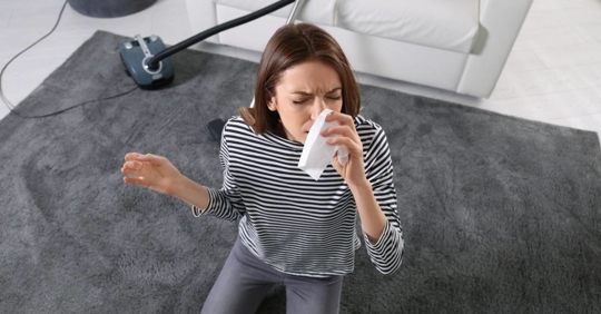 Woman suffering from dust allergy while vacuuming house